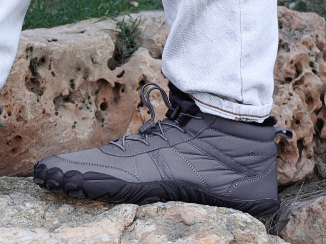 Person wearing gray hiking boots with black soles on a rocky surface