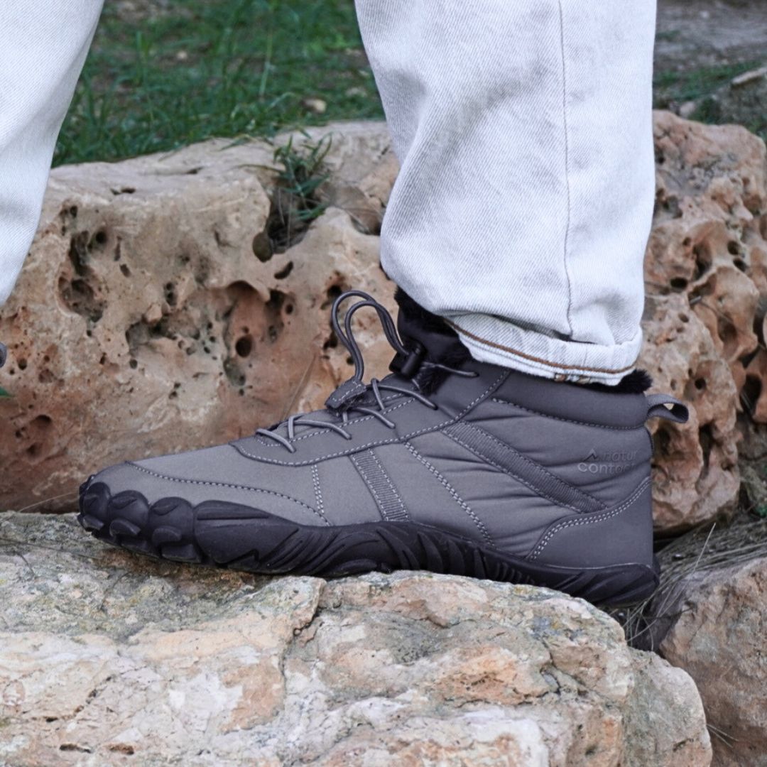 Person wearing gray hiking boots with black soles on a rocky surface