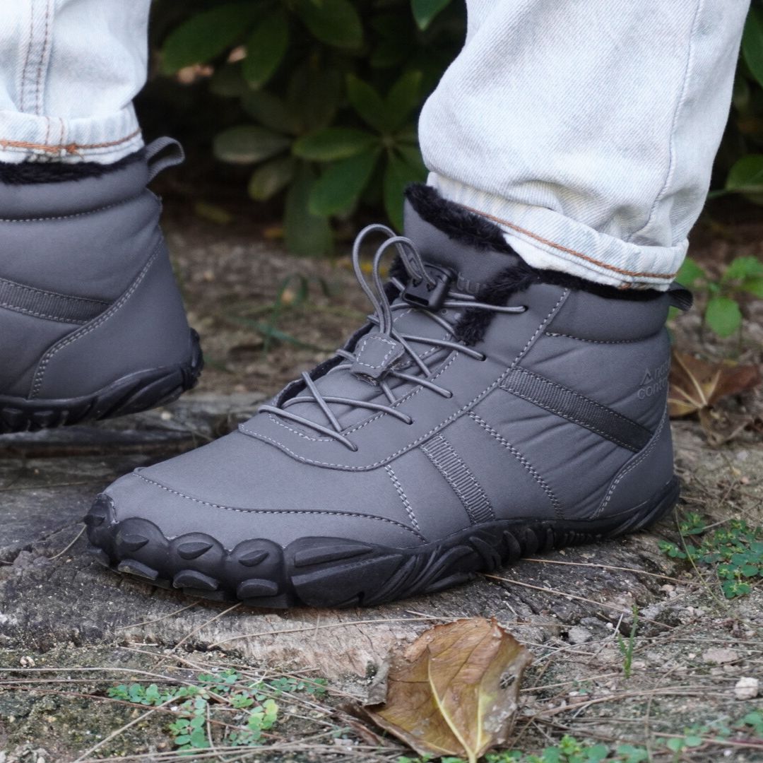 Gray winter boots with black soles worn by a person on a natural ground surface.