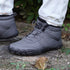 Gray winter boots with black soles worn by a person on a natural ground surface.