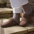 Side view of a person wearing dark brown suede clogs and white trousers, standing on rustic stone stairs.