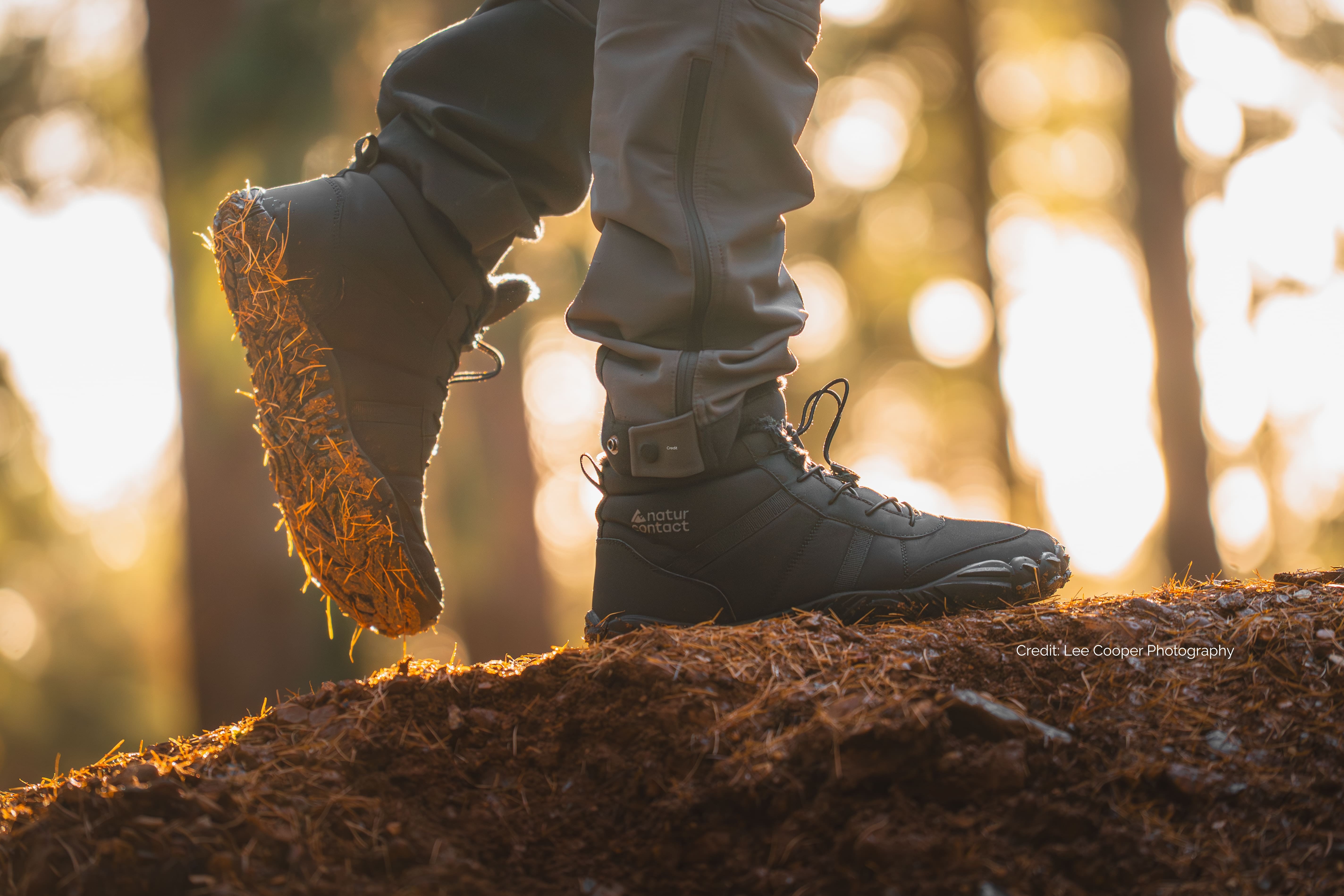 Person wearing black barefoot hiking boots shoes with naturcontact logo on a forest floor with a blurred background