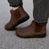 Brown ankle barefoot boots worn with gray jeans on a concrete surface