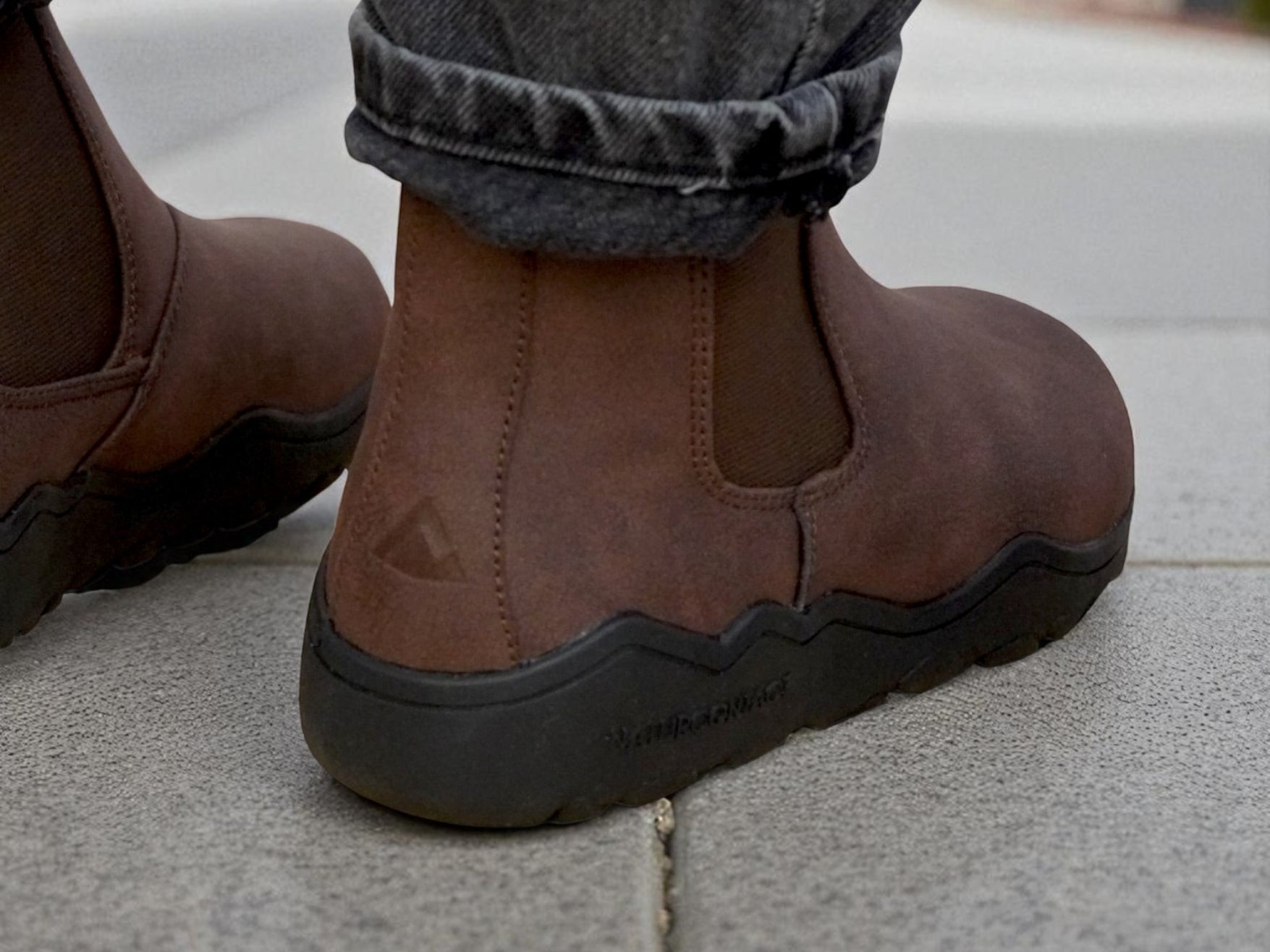 Brown barefoot boots with black soles worn on a concrete surface