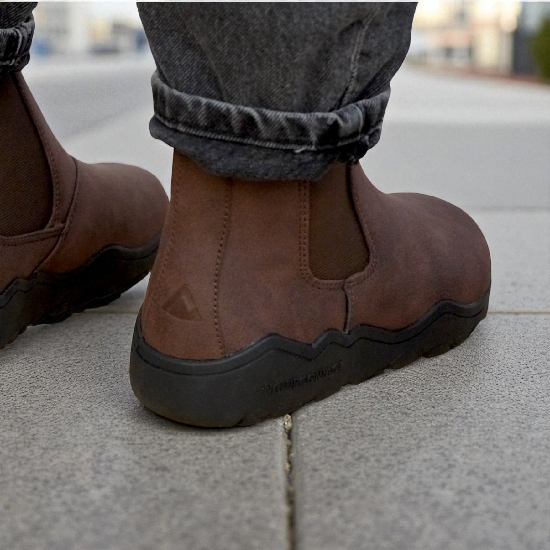 Brown barefoot boots with black soles worn on a concrete surface