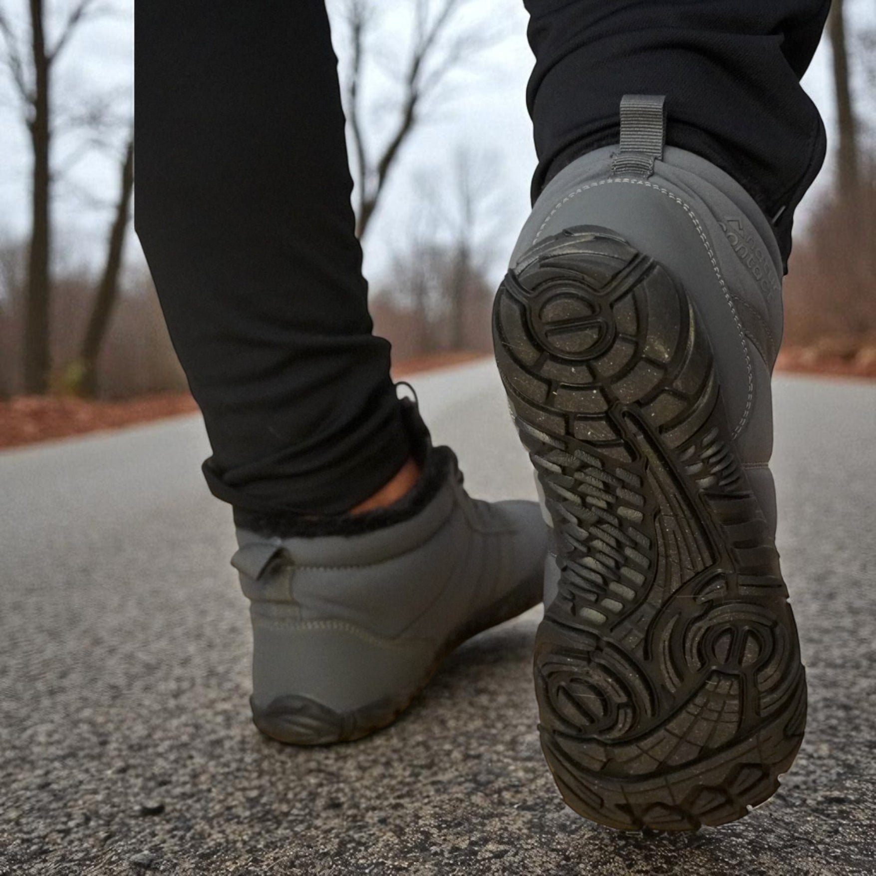 Close-up of a person wearing gray boots on a road with blurred trees in the background