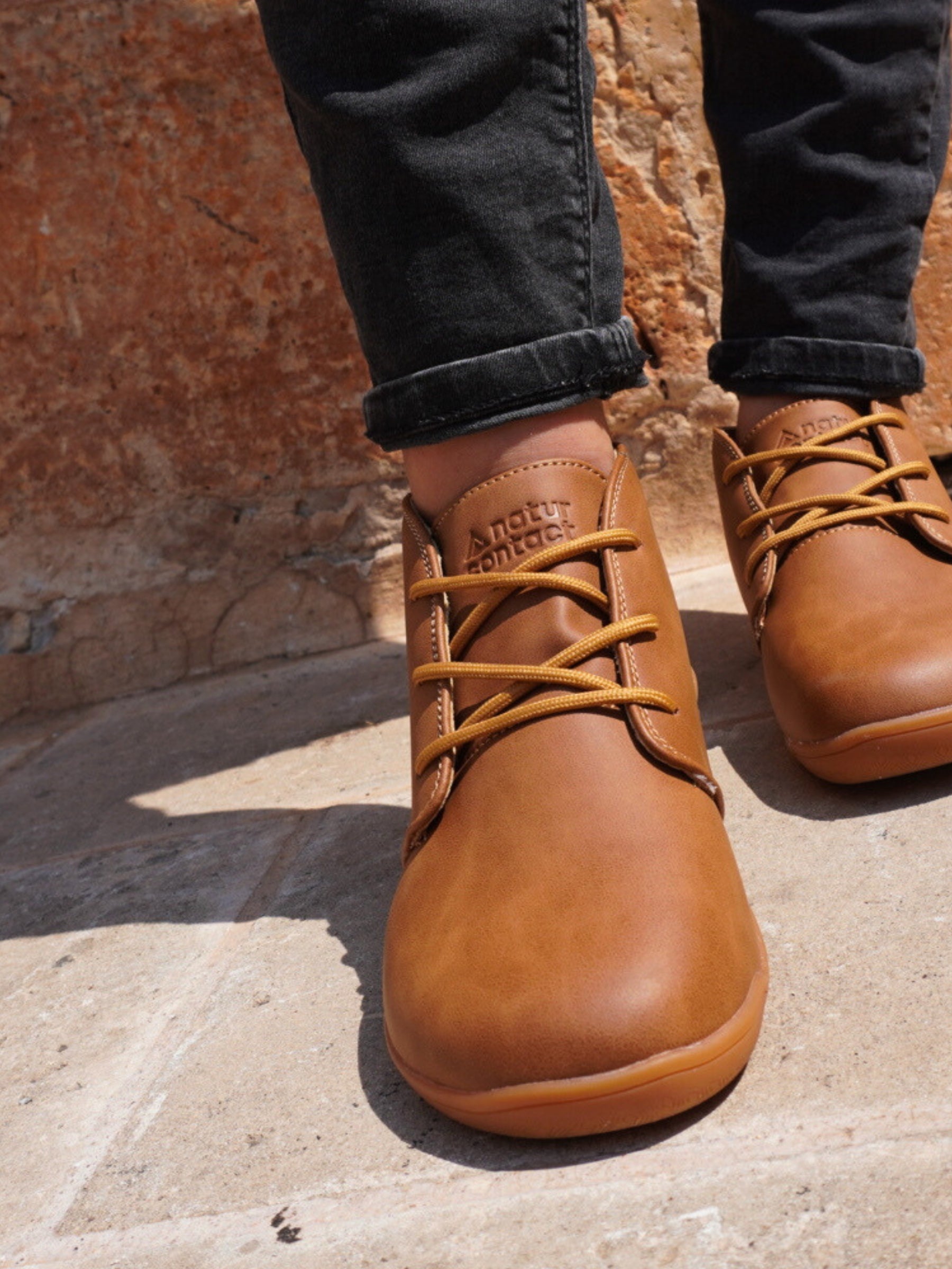 Brown leather shoes with laces worn on a stone surface.