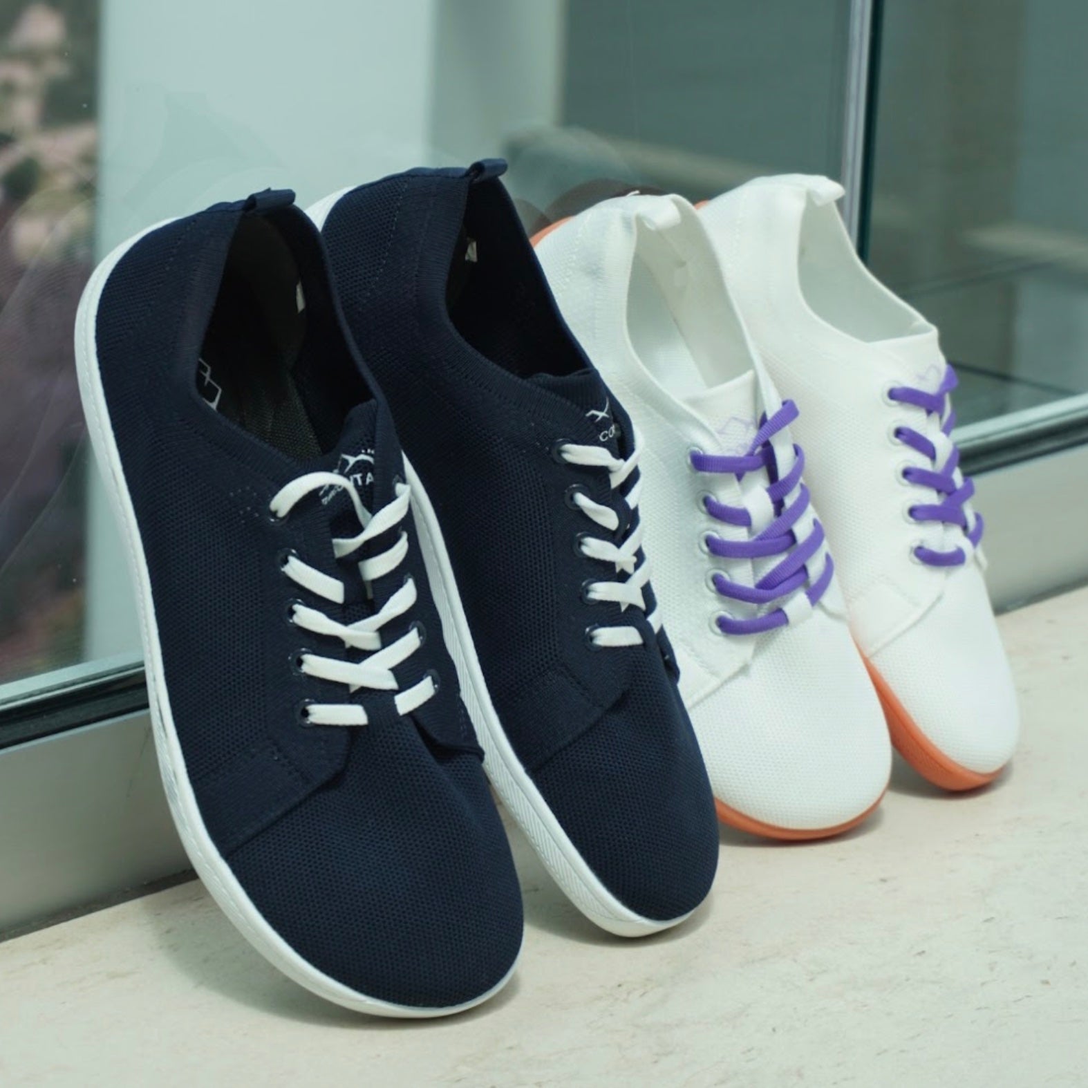 Pair of navy blue and white sneakers with a single white sneaker with purple laces on a light surface.