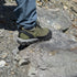 Person wearing green hiking barefoot shoes on a rocky surface