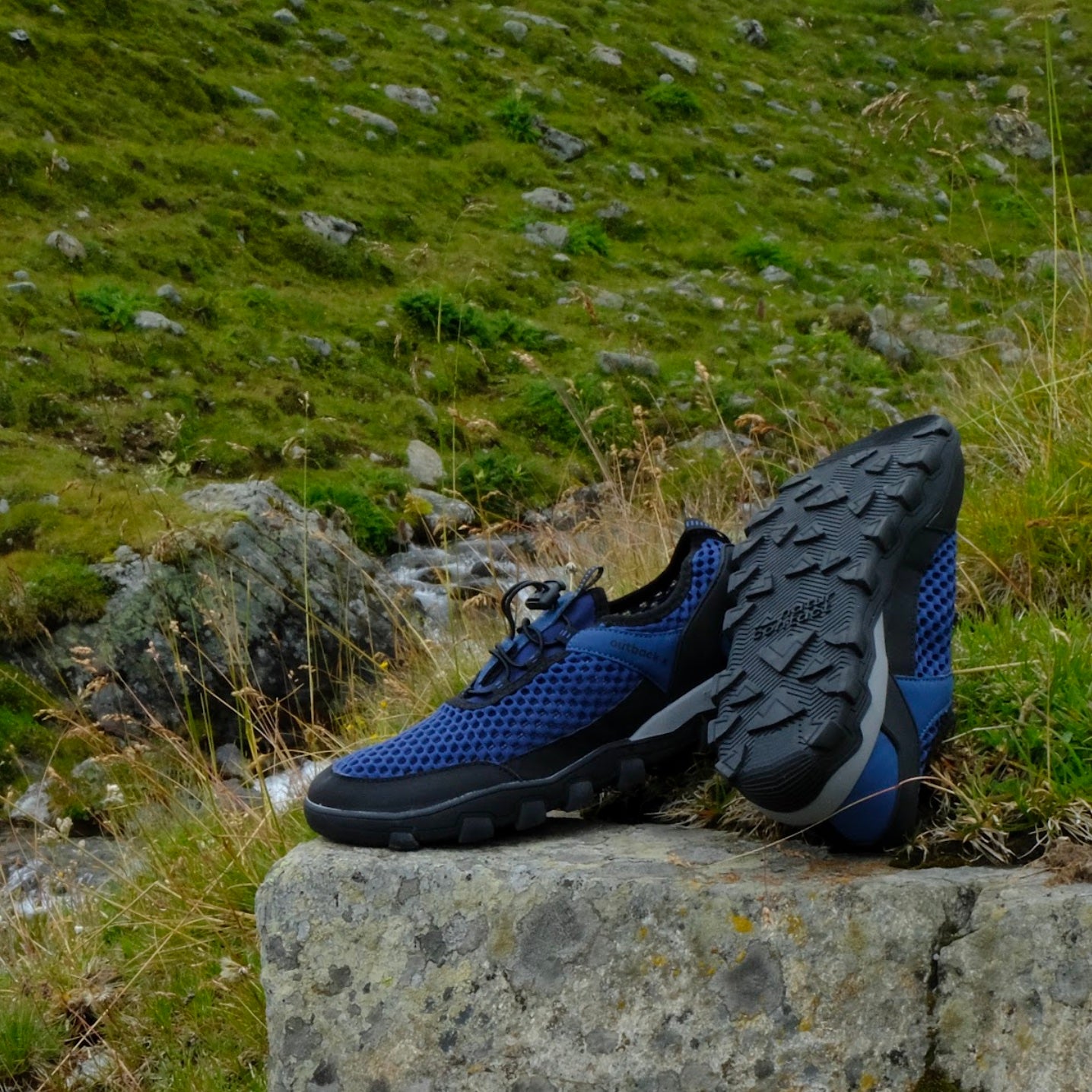 Blue and black hiking barefoot shoes on a stone ledge with a natural landscape background