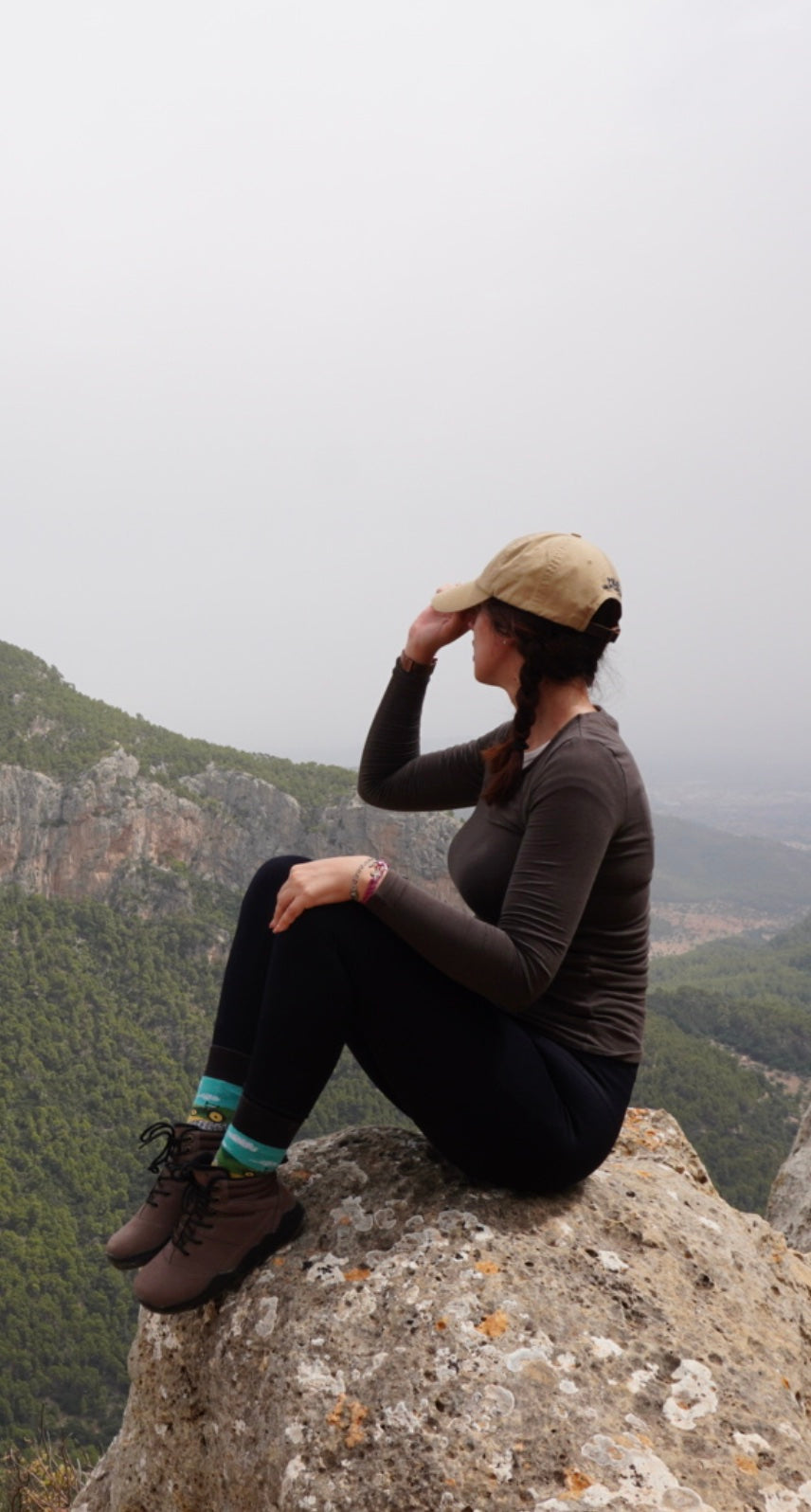 Person sitting on a rock with a mountainous landscape in the background wearing winter barefoot shoes