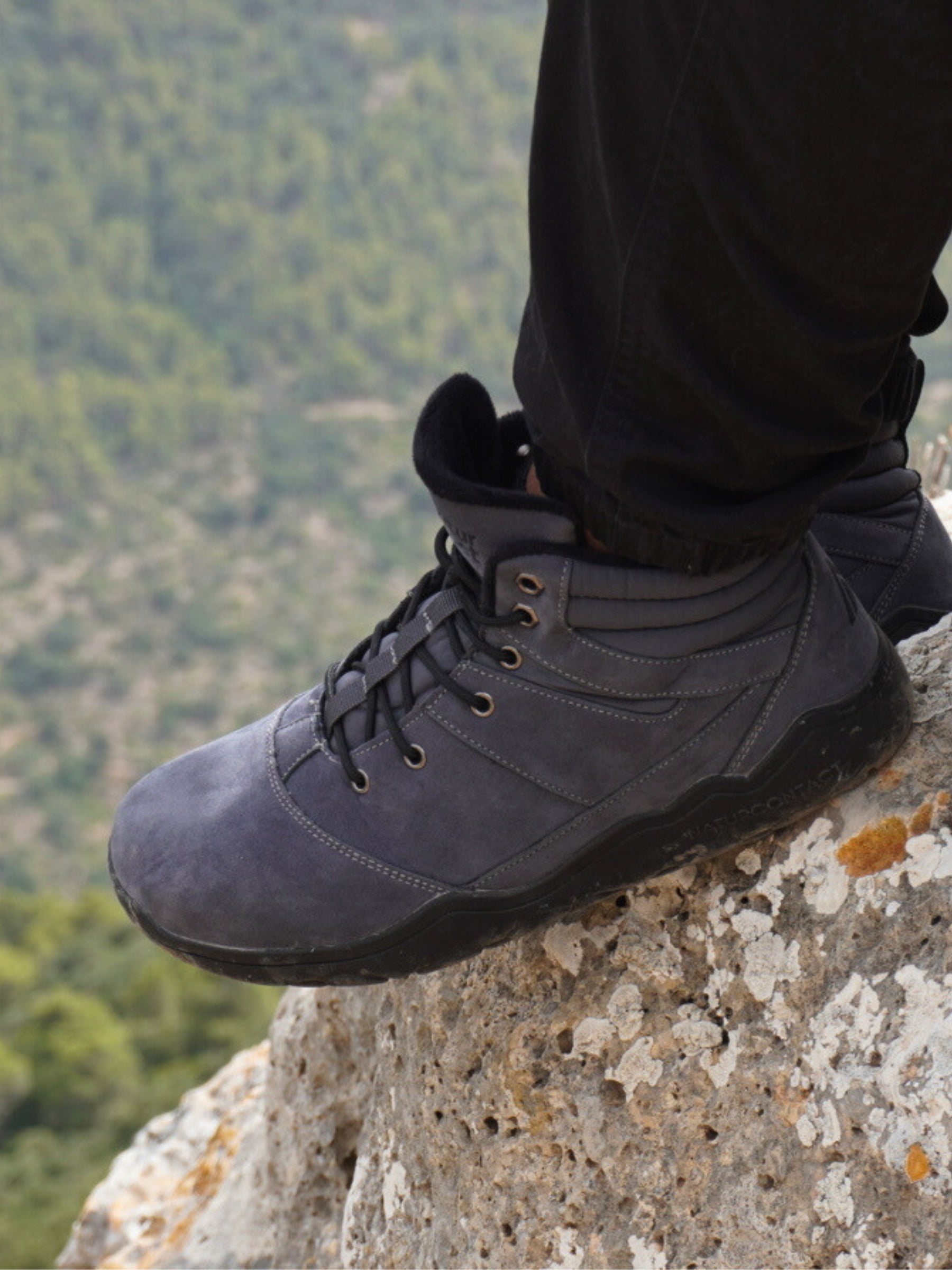 Person wearing dark gray hiking boots on a rock with a forest background