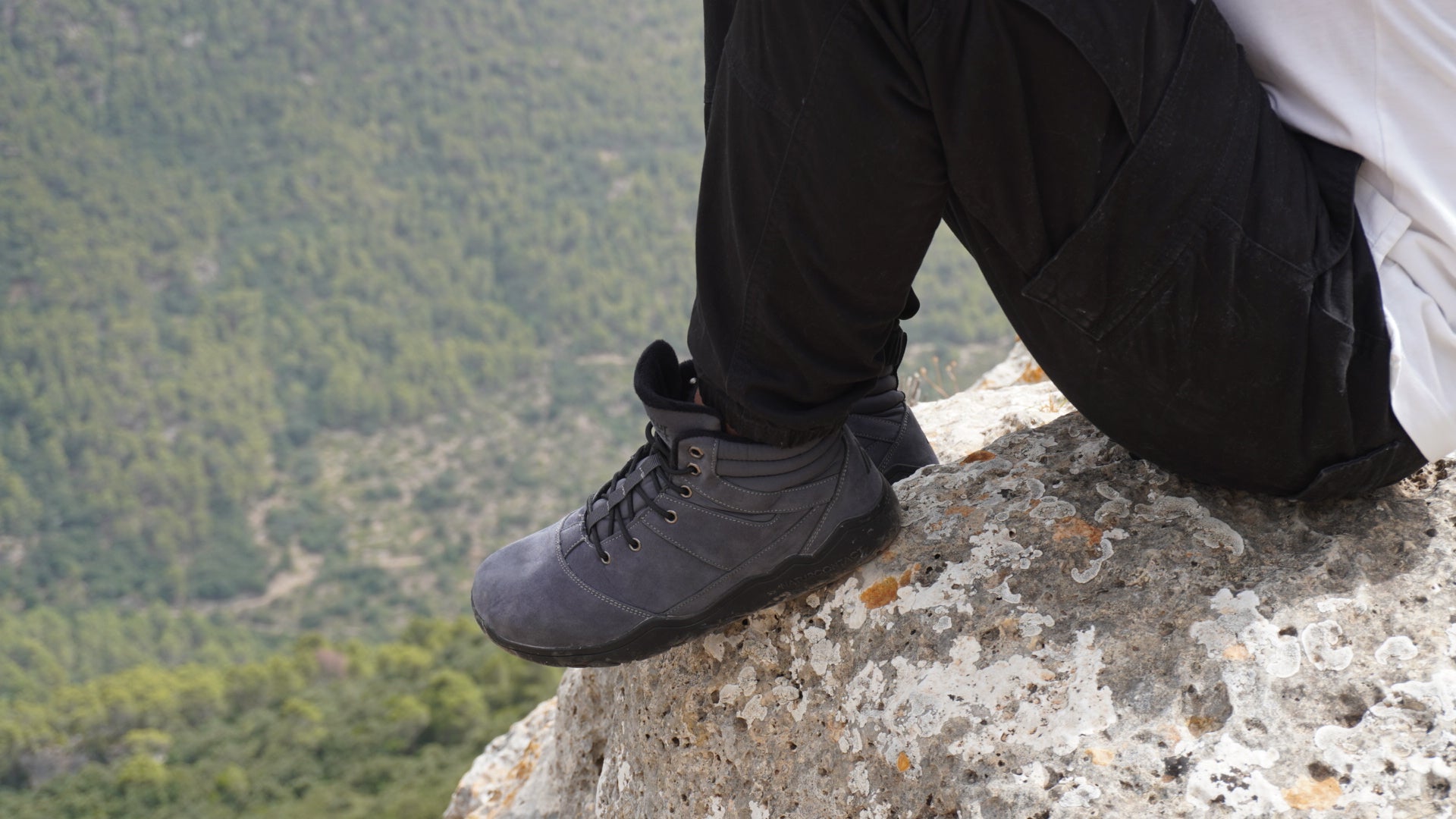 Person wearing hiking boots on a rocky outcrop with a mountainous background