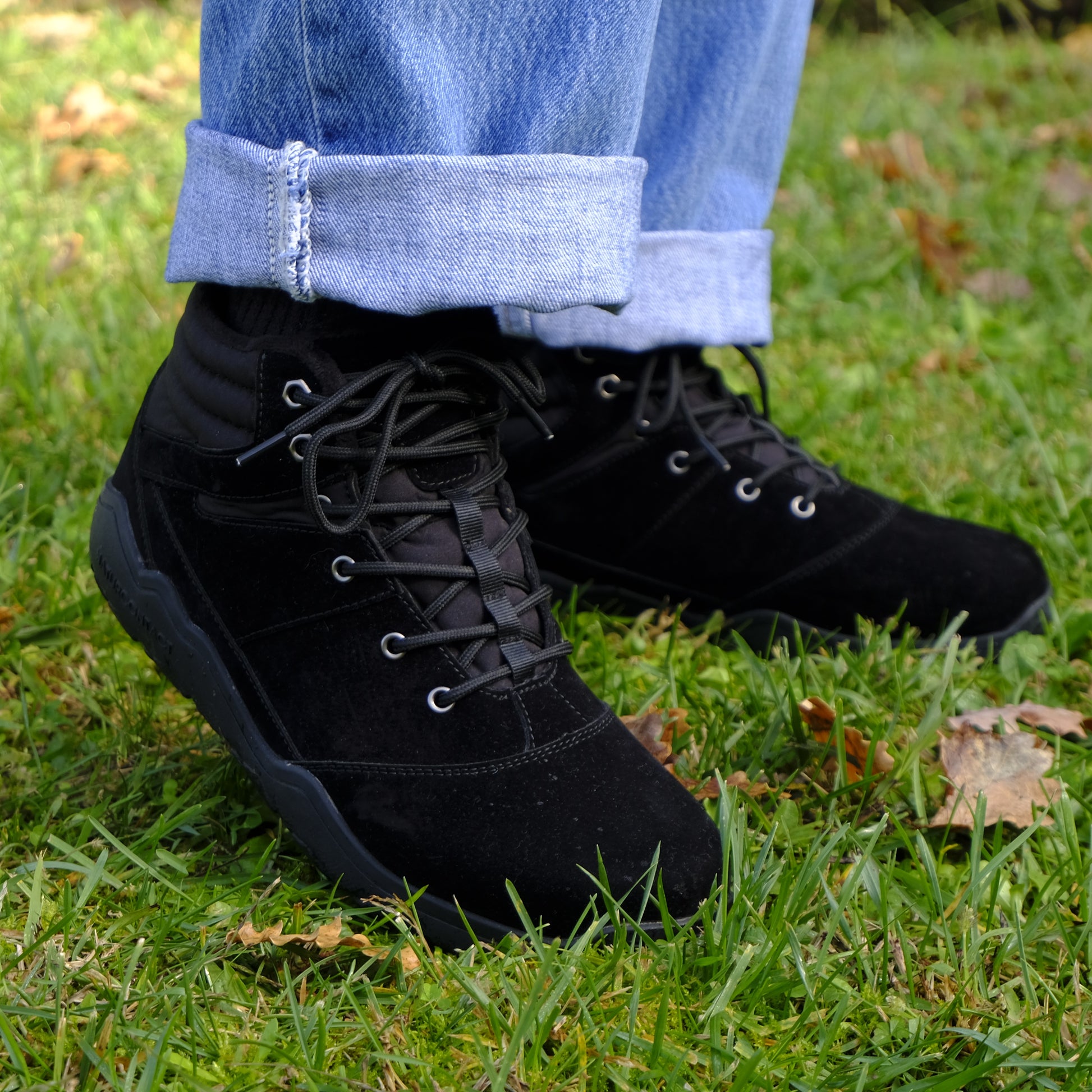 Black boots worn with rolled-up jeans on a grassy background
