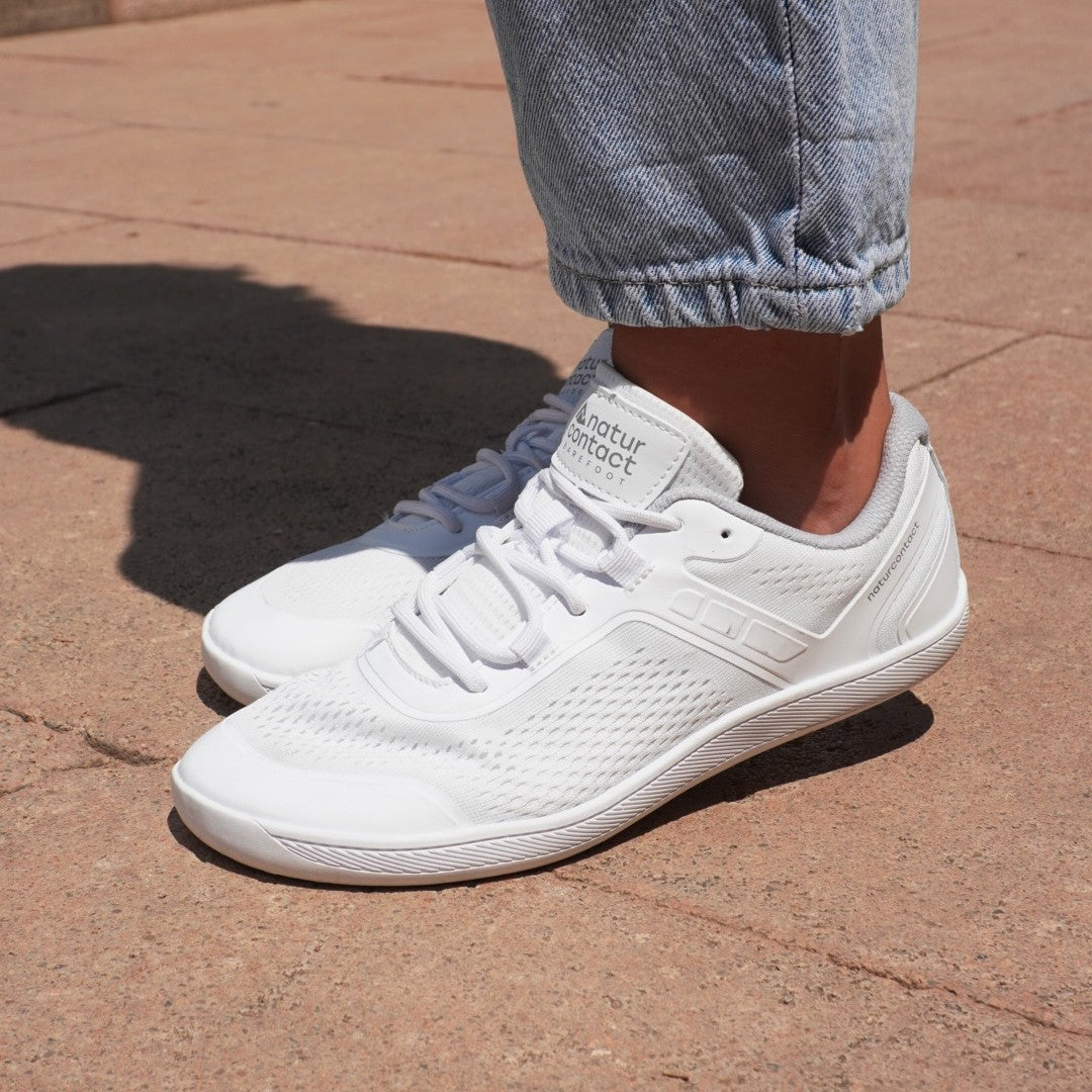 White sneakers worn with blue jeans on a brown pavement