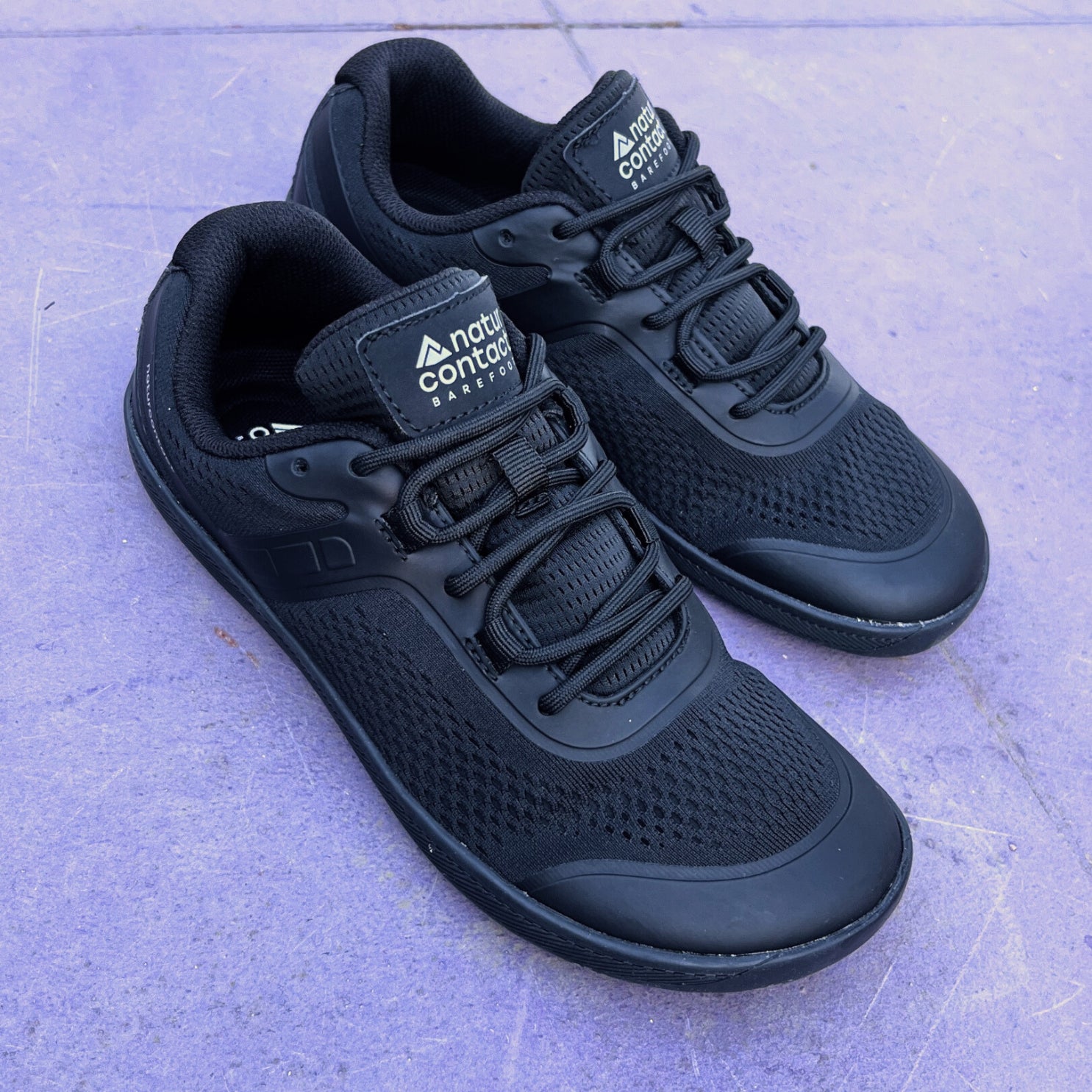 Pair of black athletic shoes with 'naturcontact' branding on a light purple surface.
