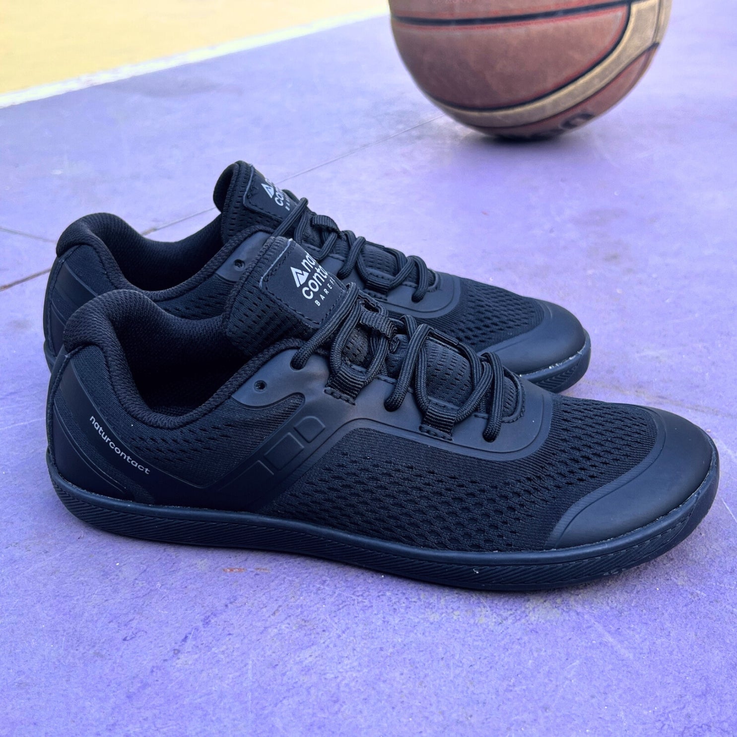 Black athletic shoes on a tiled floor with a basketball in the background