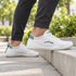 White and green Naturcontact Aramid Contact 2.0 barefoot trainers worn outdoors with dark trousers on a pavement step.