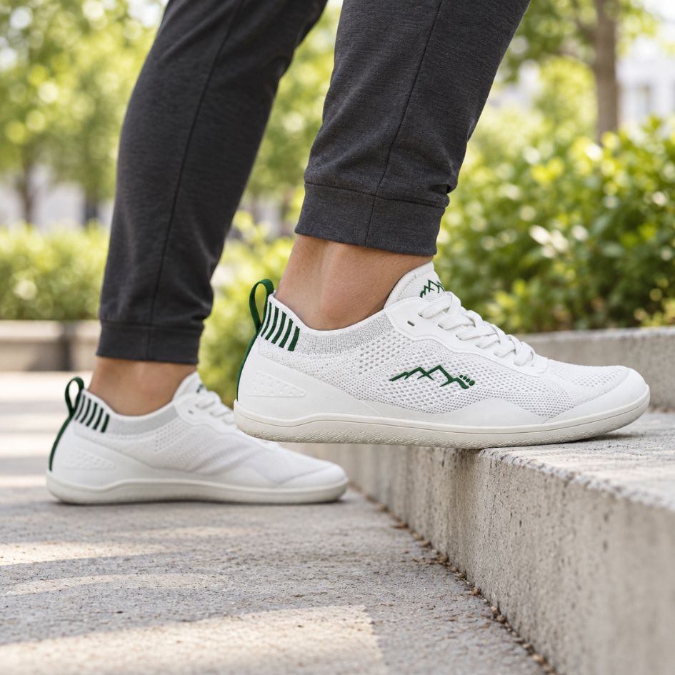 White and green Naturcontact Aramid Contact 2.0 barefoot trainers worn outdoors with dark trousers on a pavement step.