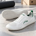 White and green Aramid Contact 2.0 barefoot trainers arranged as a pair in a minimal indoor setting, with one shoe displaying the white outsole.