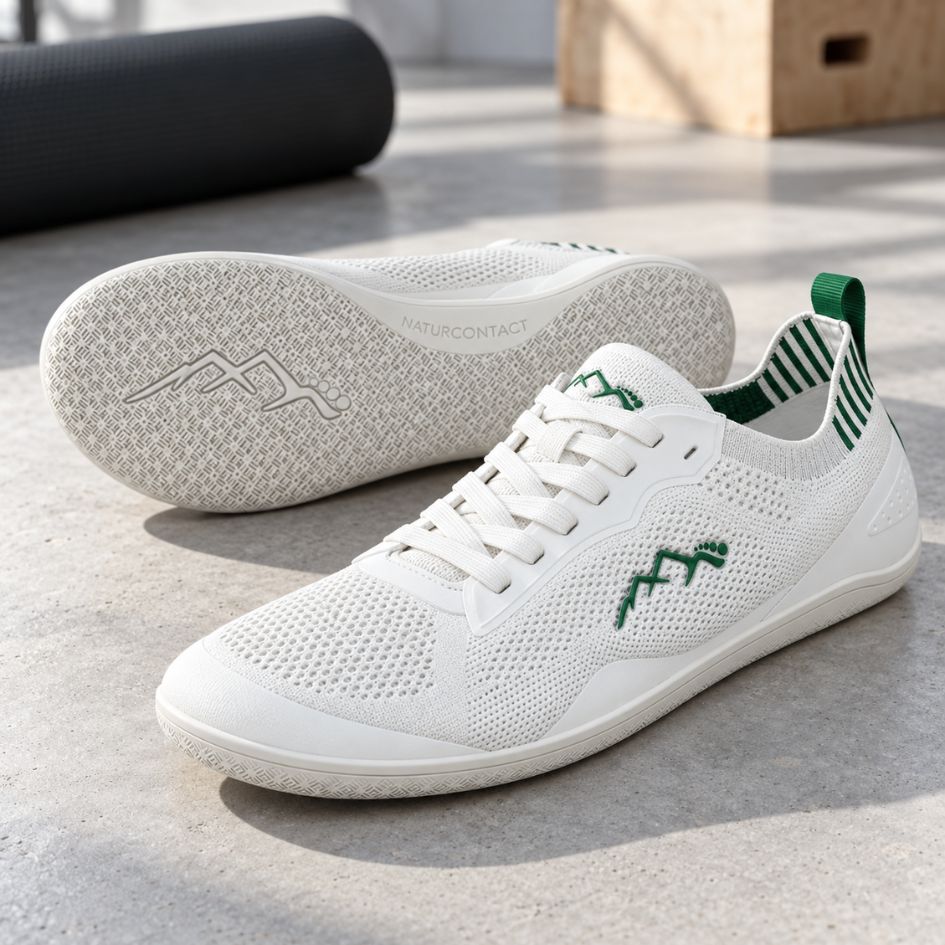 White and green Aramid Contact 2.0 barefoot trainers arranged as a pair in a minimal indoor setting, with one shoe displaying the white outsole.