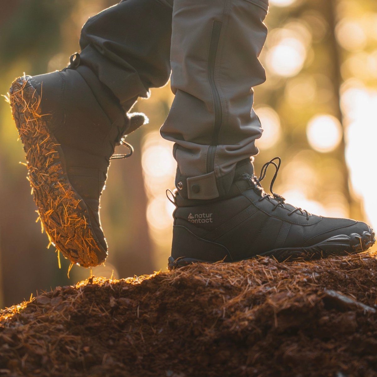 Side view of Naturcontact Arctic Contact 4.0 black barefoot winter boots while hiking on a forest trail, highlighting flexible sole, grip, and natural walking movement