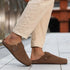 Brown barefoot suede clog worn with beige pants on a blurred outdoor background