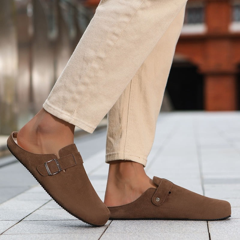 Taupe Brown barefoot suede clog worn with beige pants on a blurred outdoor background