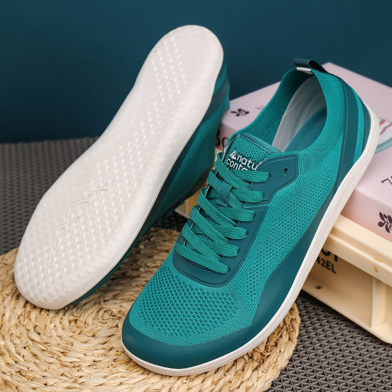 Teal barefoot sneakers with white soles on a textured surface