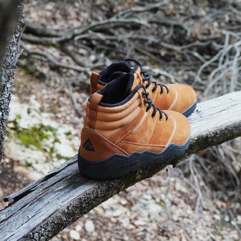 Naturcontact Intemperia 2.0 winter barefoot boots in brown placed on a tree branch, outdoor use with flexible sole and natural movement design