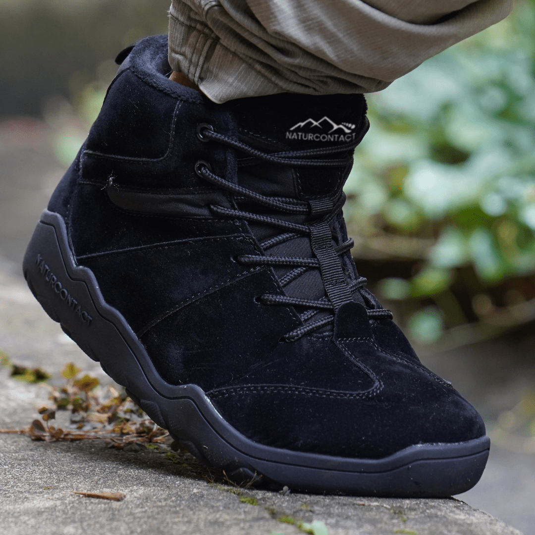 Naturcontact Intemperia winter barefoot boots in Black suede, worn outdoors on stone surface, featuring zero drop sole, wide toe box and flexible minimalist design for cold weather.