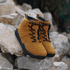 Pair of Naturcontact Intemperia winter barefoot boots in Gold color, with wide toe box, flexible sole and suede upper, placed on rocks in an outdoor setting.