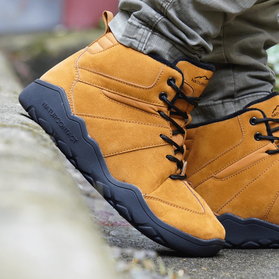 Side view of Naturcontact Intemperia winter barefoot boots in Gold, showing the flexible sole, suede upper and outdoor grip while walking on stone.