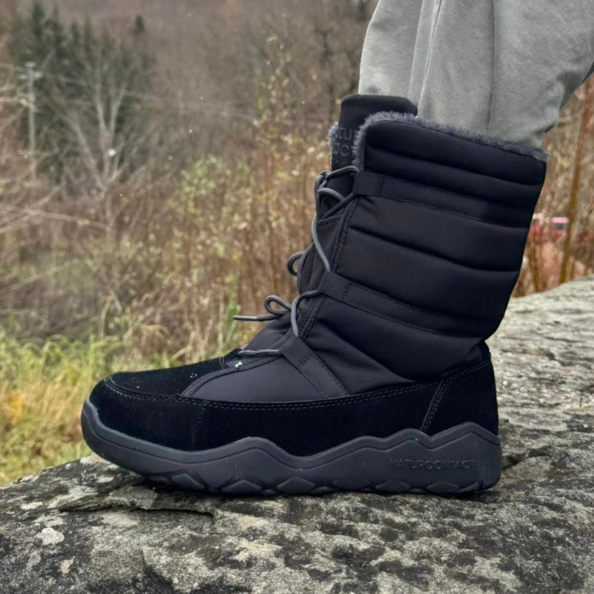 Black Naturcontact Lapland high-top winter barefoot boots worn outdoors on rocky terrain, showing flexible sole and insulated design