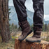 Brown Naturcontact men’s winter barefoot boots worn outdoors on a tree stump in a mountain landscape