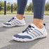 White and navy Sport Contact 2.0 barefoot trainers worn outdoors with blue-grey leggings, showing their low-profile shape.