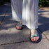 Person wearing barefoot sandals and white striped pants on a stone pavement.