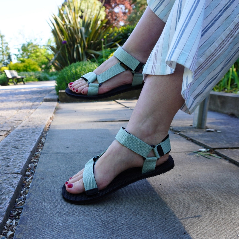 Person wearing  barefoot sandals on a stone path with plants in the background