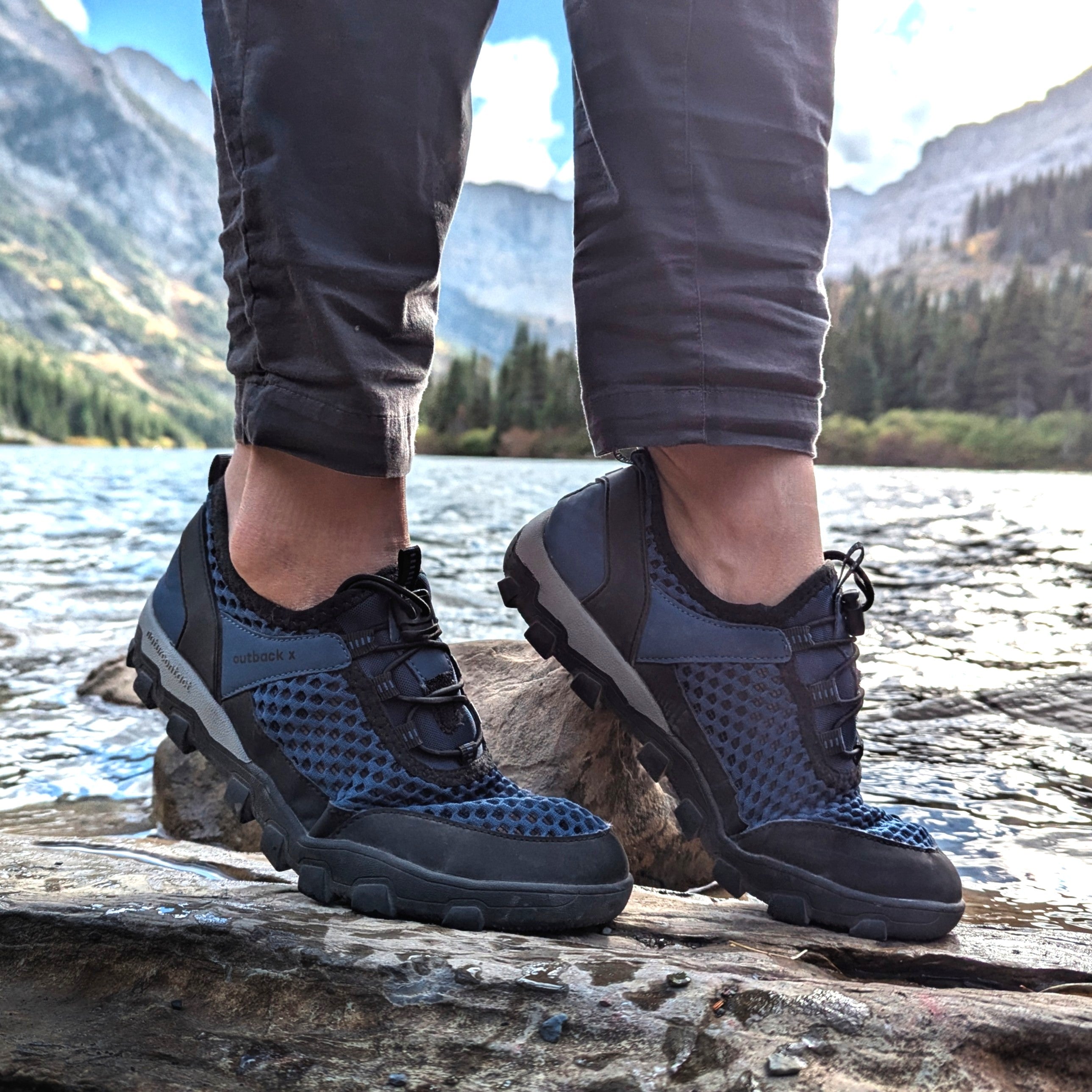 Person wearing black and gray hiking shoes with a mountainous landscape in the background