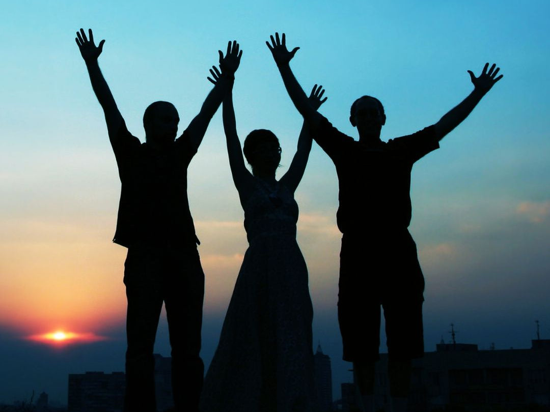 Silhouettes of three people with raised arms against a sunset sky