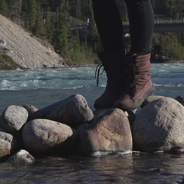 person walking in brown barefoot high top boots on rocks in a river
