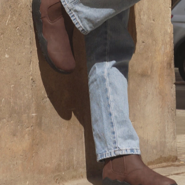 person in jeans next to a wall showing brown barefoot chelsea boots in jeans