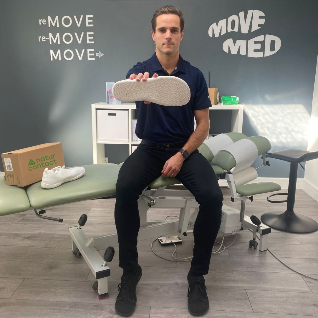 Man holding a shoe in a medical office with 'MOVE MED' branding and with naturcontact barefoot shoes