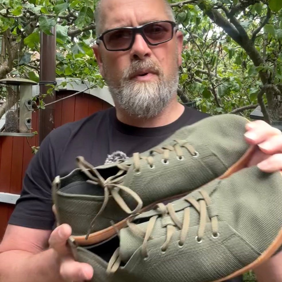 Man holding a pair of green barefoot shoes urban breeze outdoors with trees in the background