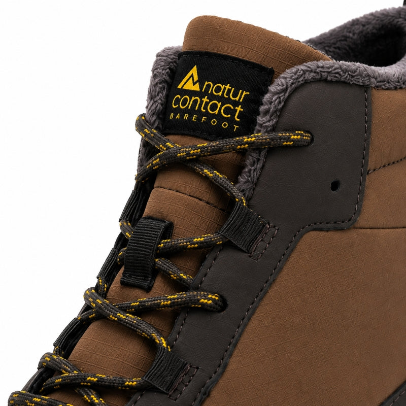 Close-up of a brown and dark gray barefoot boot with yellow and black laces, featuring a black tongue label with the 'natur contact BAREFOOT' logo.