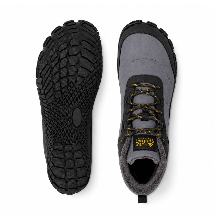 A pair of gray and black mid-height hiking boots shown from the top, displaying the treaded black outsole on the left and the side profile with yellow laces on the right. The brand 'Anvil' is visible on the tongue label.