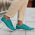 Teal barefoot sneakers worn with beige pants on a tiled floor