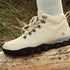 Beige hiking boot with black sole on a wooden log, grassy background