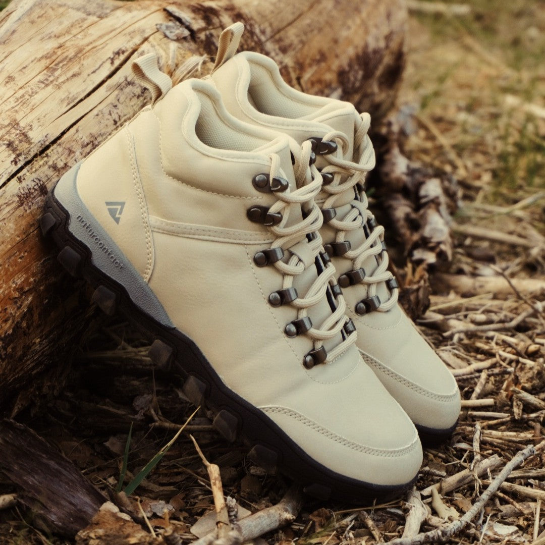 Pair of beige hiking boots on a natural background with wood and grass.