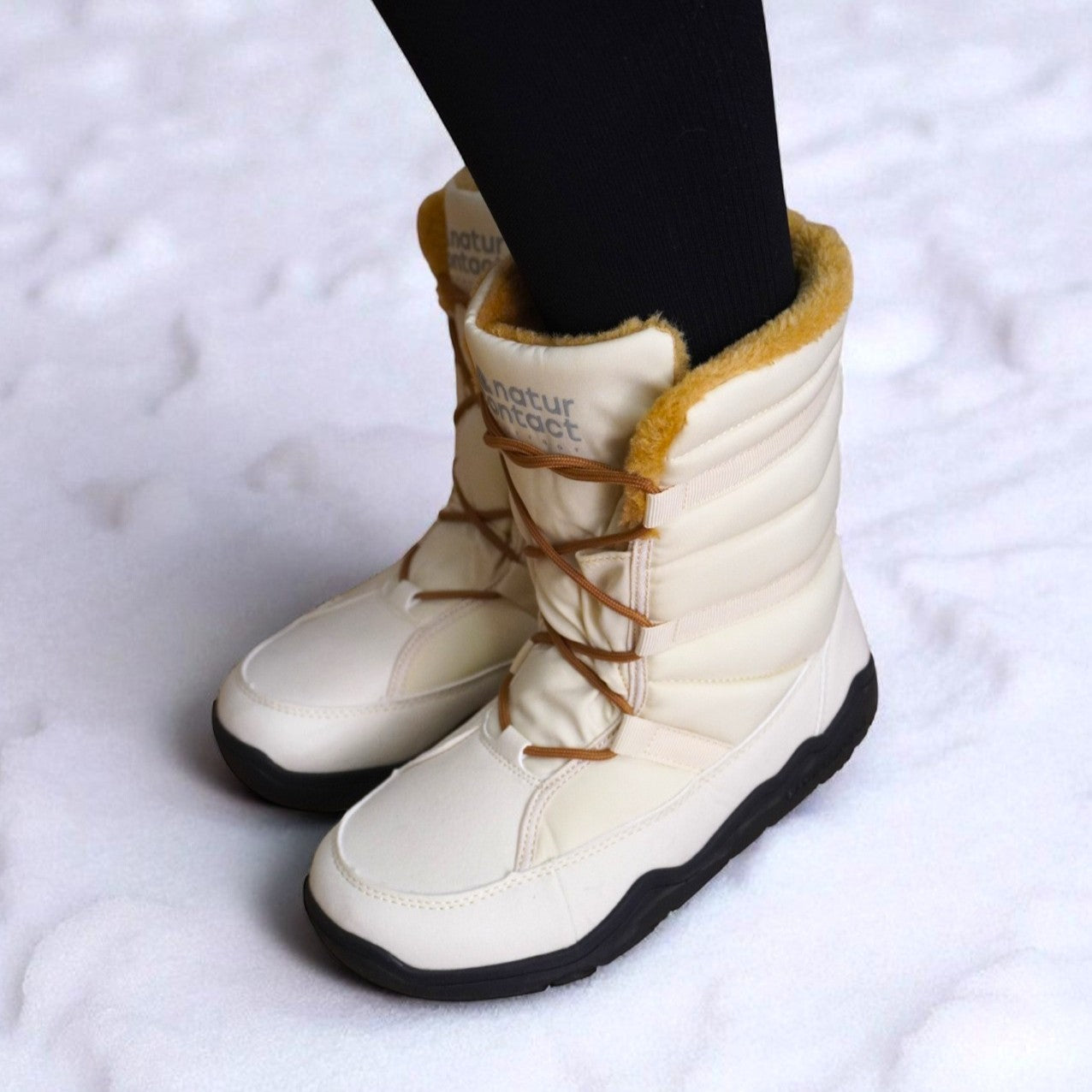 Beige Naturcontact winter boots with brown laces and golden faux fur lining, worn on snow, featuring a padded upper and black sole